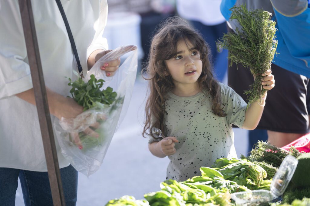 Candid photo of mother and 5 years old daughter choosing vegetables in farmer's market. Shot in outdoor with a full frame mirrorless camera.